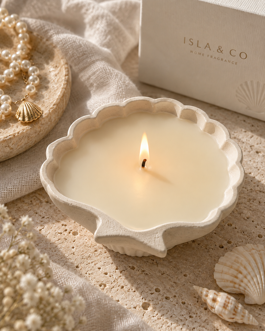 The Pearl Candle in a sculptural scallop shell vessel, lit in a warm coastal setting