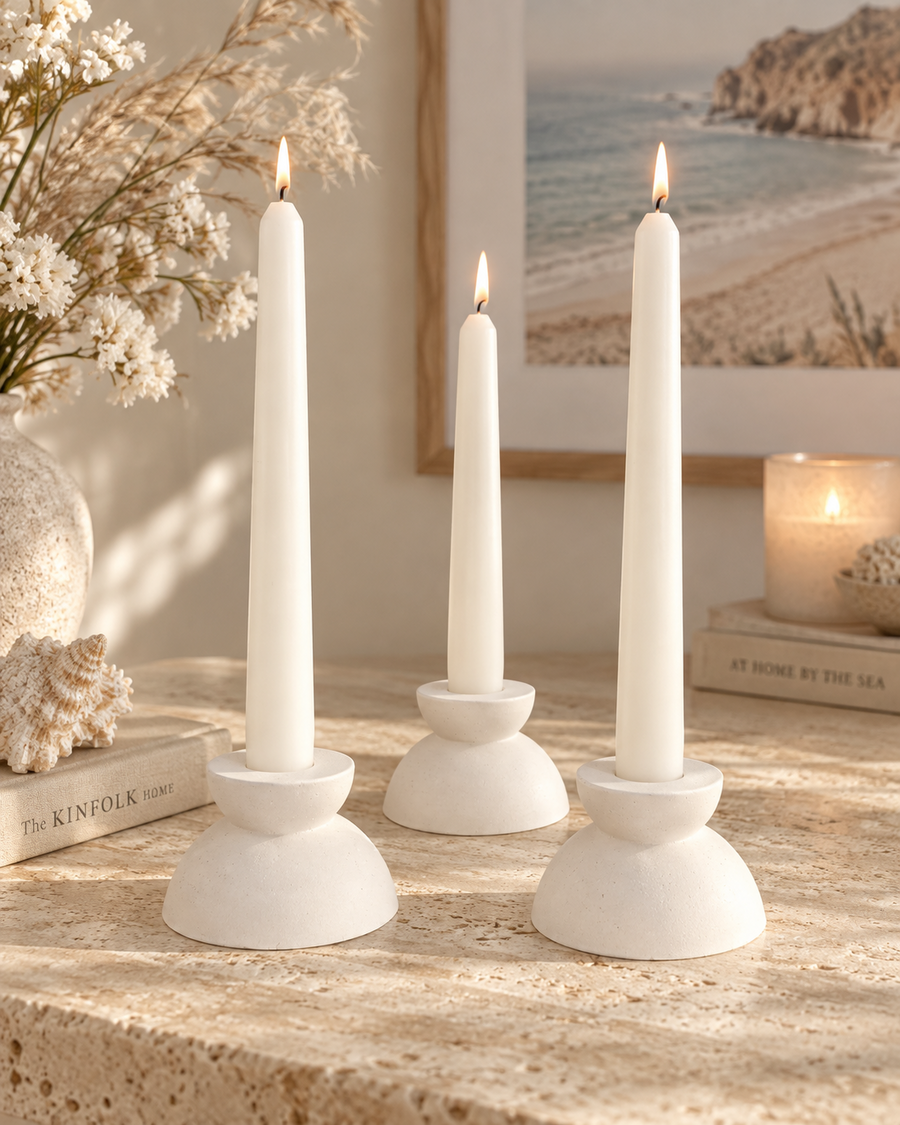 Three white stone candlestick holders with taper candles in a coastal interior